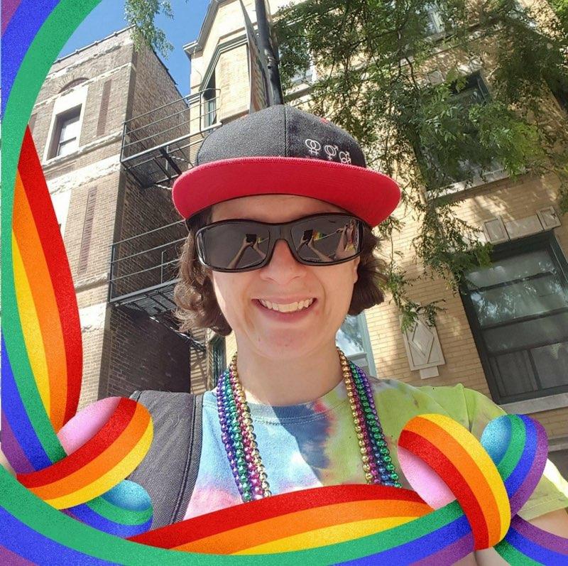 A supplied outdoor portrait with sunglasses, a cap, colorful bead necklaces, a tie-dye shirt, and a rainbow ribbon frame.